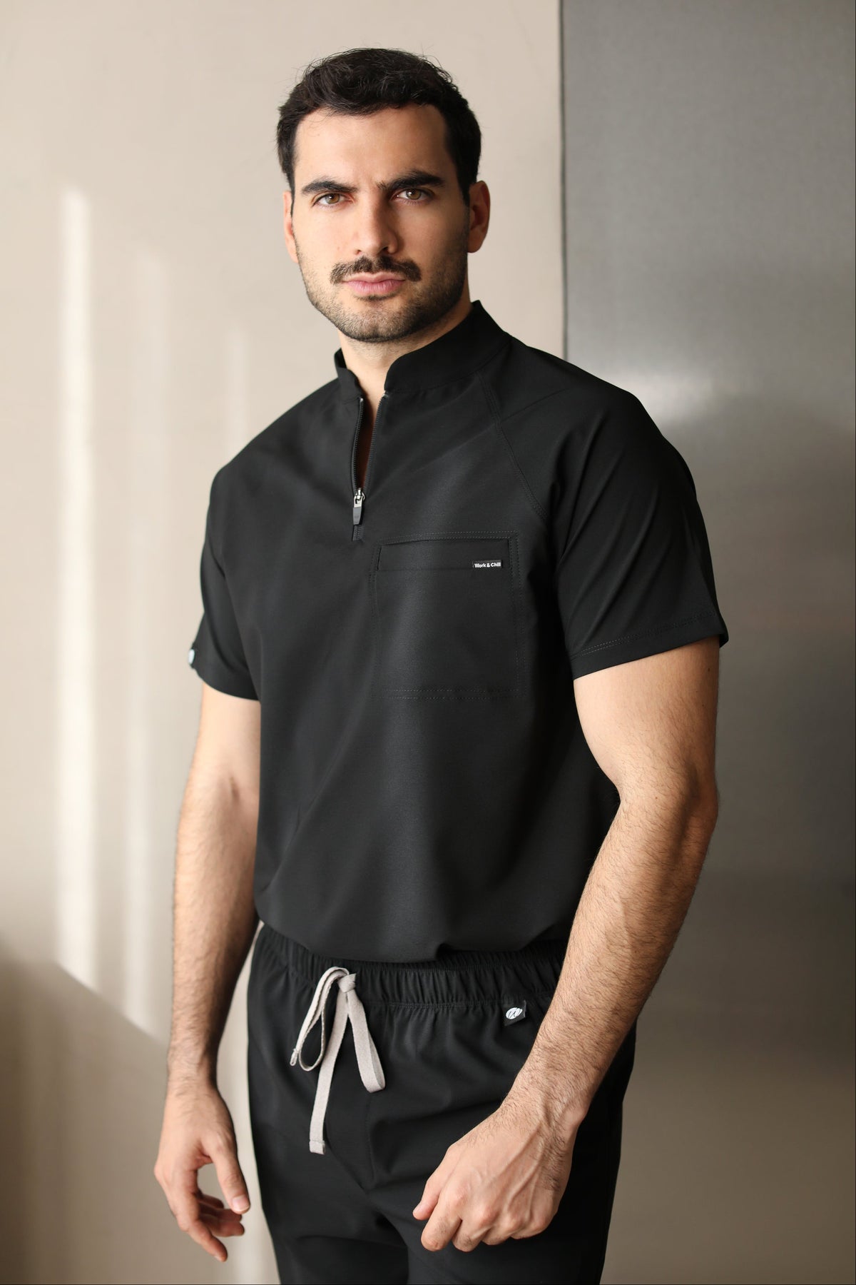 Man wearing the Harry Black W&C Shield™ scrub top and black scrub pants, shown in a front-facing three-quarter view.