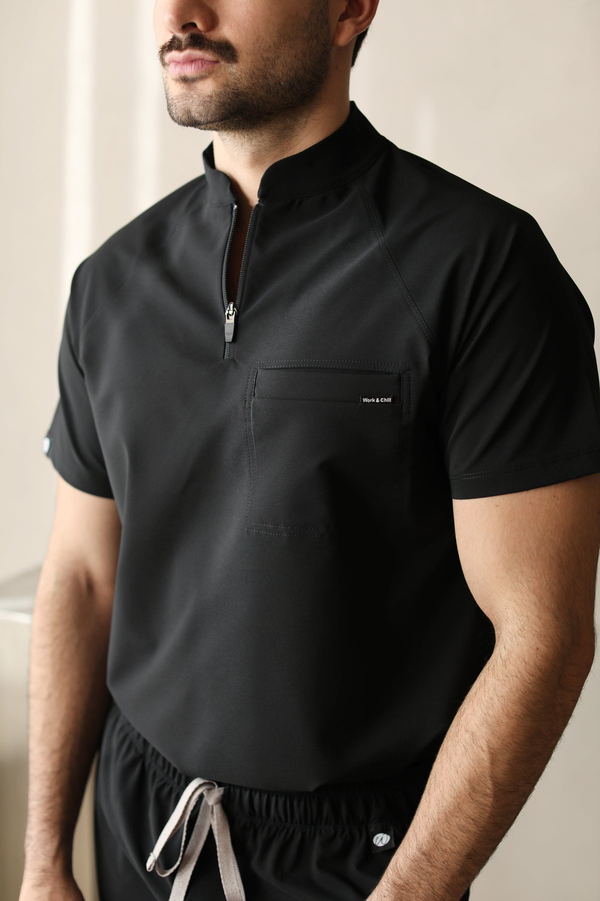 Close-up of a man wearing the Harry Black W&C Shield™ scrub top, highlighting the high collar, front zipper, and chest pocket.