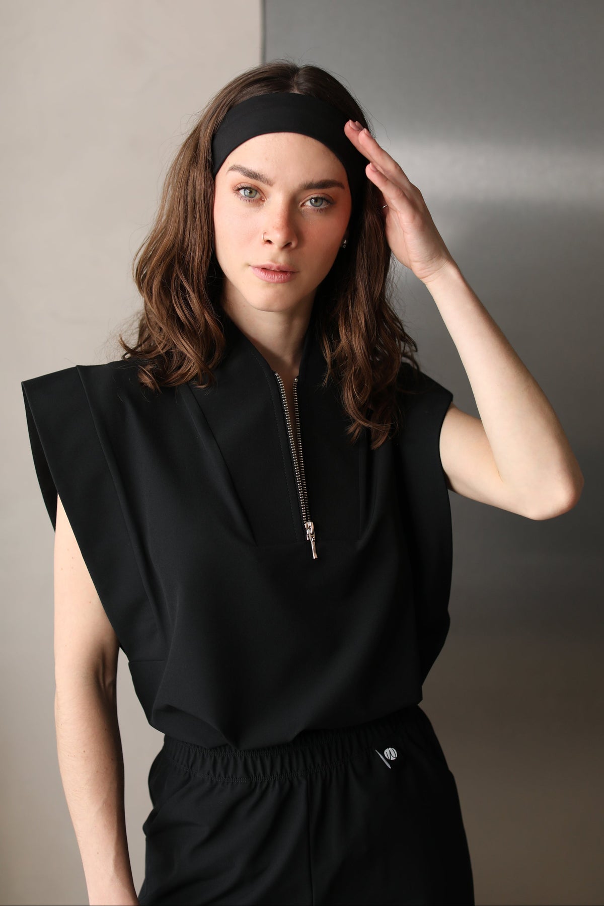Woman wearing the Kate Black W&C Shield™ scrub top, shown from the waist up with one hand touching her headband.